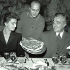 foto Ezio Vitale, Sophia Loren e Vittorio De Sica accolgono, sorridenti, una gustosa pizza napoletana, 1960 circa, bianco e nero. Al ristorante Vesuvio di Napoli