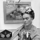 FRIDA. VIVA LA VIDA, La pittrice messicana Frida Kahlo (1907 - 1954) siede con le braccia conserte, guardando in basso, di fronte a uno dei suoi dipinti e una gabbia per uccelli in legno. Indossa fiori tra i capelli e una collana di legno | Foto: Hulton Archive - Getty Images | Courtesy of Ballandi Arts e Nexo Digital 2019