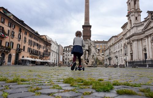 Roma, 18 aprile 2020. In una Piazza Navona deserta, con l’erba che cresce tra i sampietrini, una bambina corre in monopattino dopo la decisione del governo di permettere brevi uscite per fare esercizio fisico