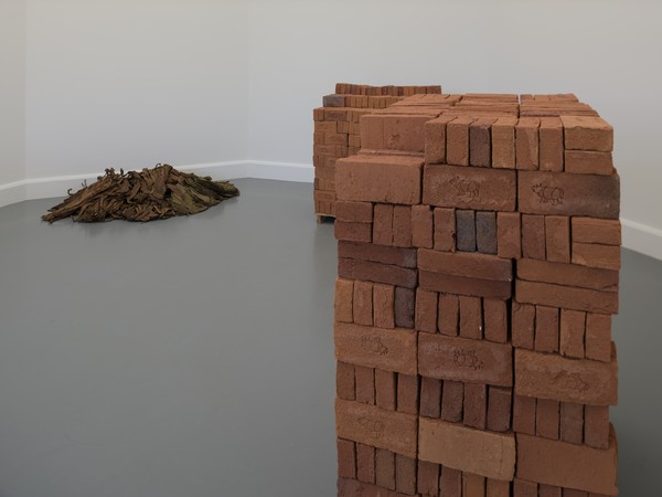 Captions Rossella Biscotti, Clara, 2016 (60 pounds of straw, 40 pounds of bread, 14 buckets of water). Installation with custom made bricks, tobacco, pallets and wall text in vinyl