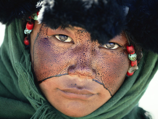 Una ragazza nomade con il volto cosparso di una sostanza protettiva durante un pellegrinaggio Tibet, Cina 1990. © Kazuyoshi Nomachi