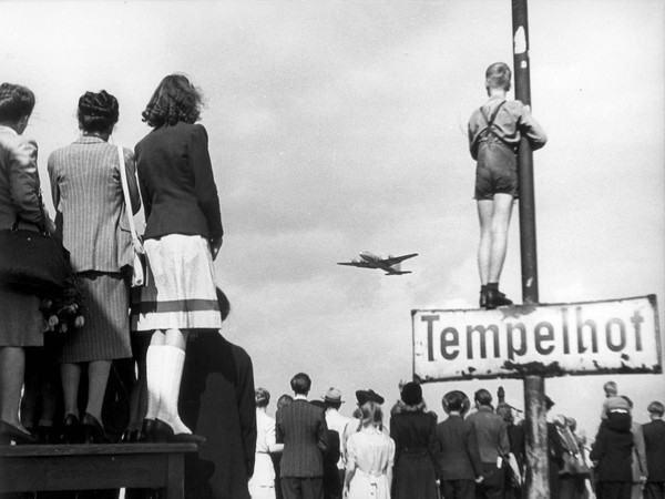 Berlinesi guardano atterrare all'aeroporto di Templehof uno dei velivoli del ponte aereo organizzato da Stati Uniti, Francia e Gran Bretagna per rifornire la popolazione durante il blocco della città. 1948, Berlino