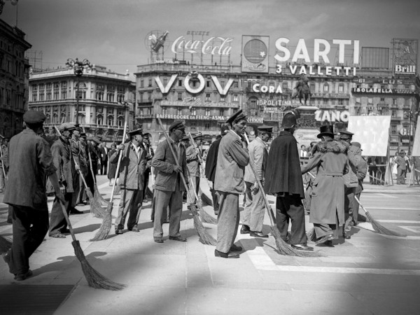 Comparse che interpretano degli spazzini fotografate in Piazza del Duomo durante la lavorazione di una scena del film Miracolo a Milano di Vittorio De Sica, 1951