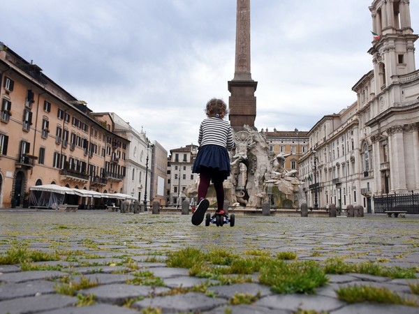 Roma, 18 aprile 2020. In una Piazza Navona deserta, con l’erba che cresce tra i sampietrini, una bambina corre in monopattino dopo la decisione del governo di permettere brevi uscite per fare esercizio fisico