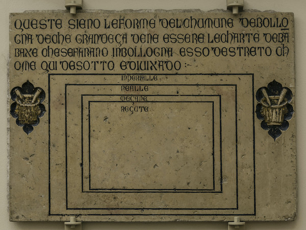 Lapide Società degli Speziali XIV-XV sec. Pietra d'Istria, cm 75 x 103 x 3,5 Bassorilievo. Iscrizione incisa in scrittura maiuscola gotica: specchio epigrafe principale cm 22 x 113; altezza delle lettere cm. 3,5 e cm 2 Bologna, Lapidario del Museo Ci