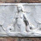 Targa con Sirena bicaudata, Palazzetto in Via dei Rossi, Siena | foto: Sailko (Opera propria) via Wikimedia Creative Commons | La sirena a due code di epoca medievale scolpita in moltissimi luoghi di culto e non solo, risale ad una simbologia millenaria legata all'antichissimo Culto della Dea Madre diffuso nell’Europa Neolitica oltre che ai più recenti culti di alcune divinità egizie come Api e Bastet.